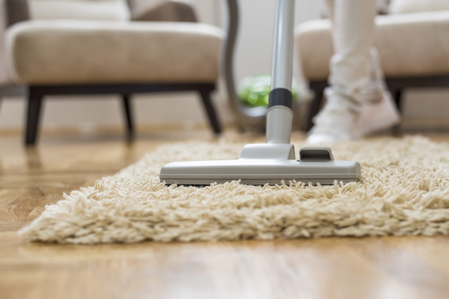Vacuum cleaner cleaning a beige carpet on wooden floor.