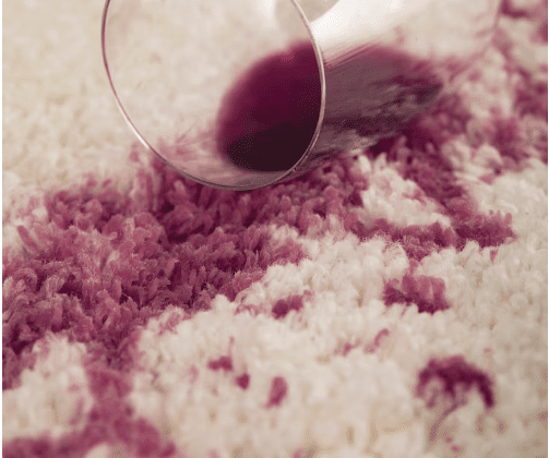 Red wine spilled on a light-colored carpet from a tipped glass.