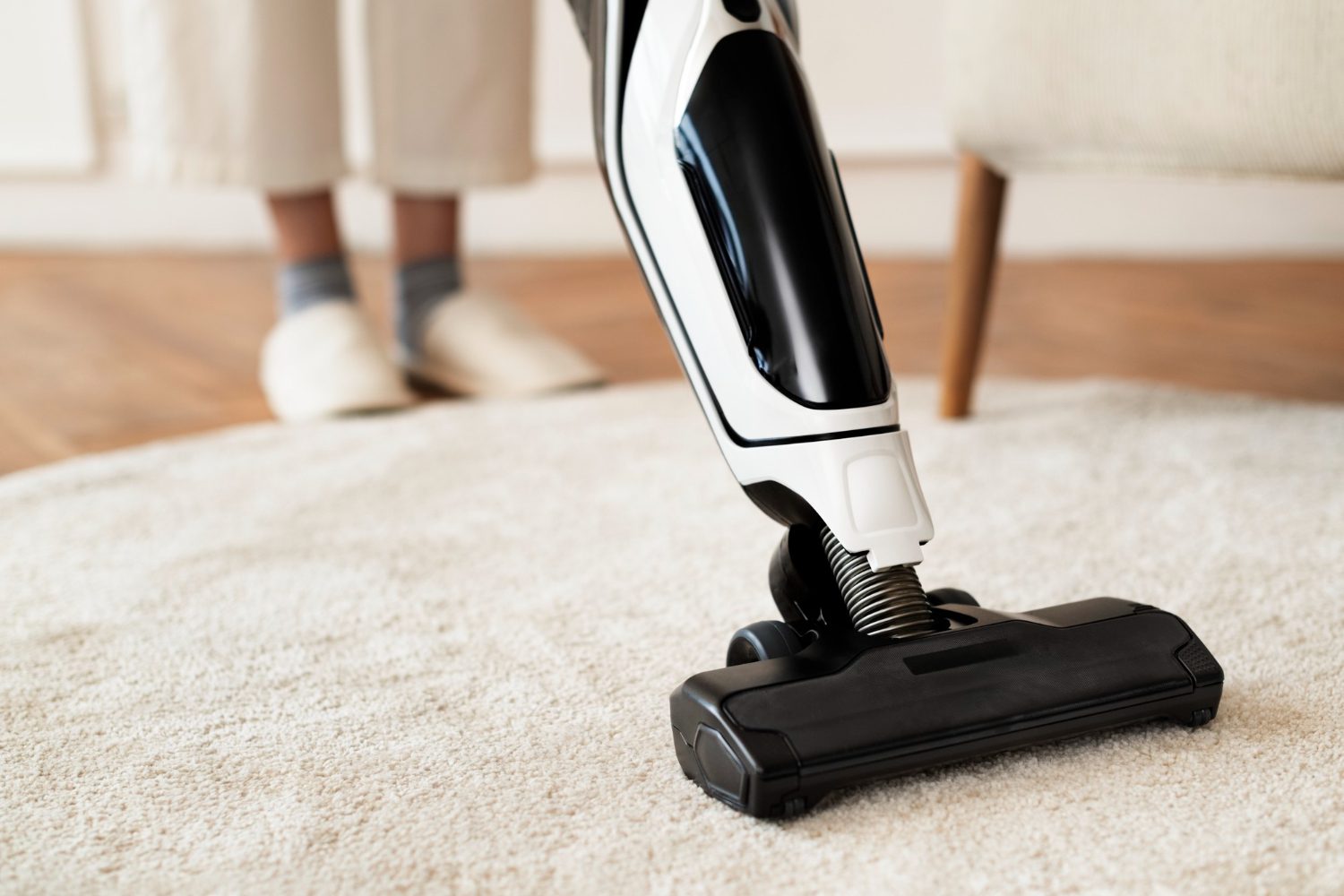 Person vacuuming a beige carpet with a modern vacuum cleaner.