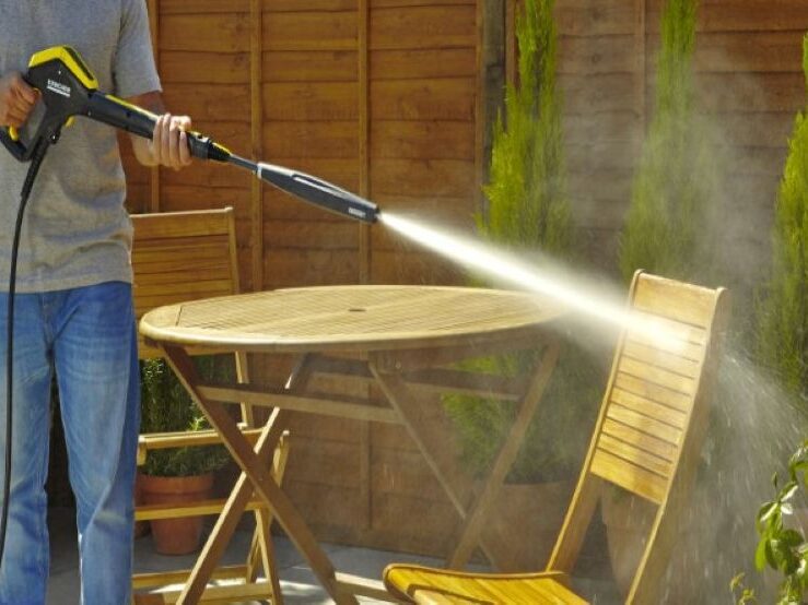 Person pressure washing a wooden table outdoors.