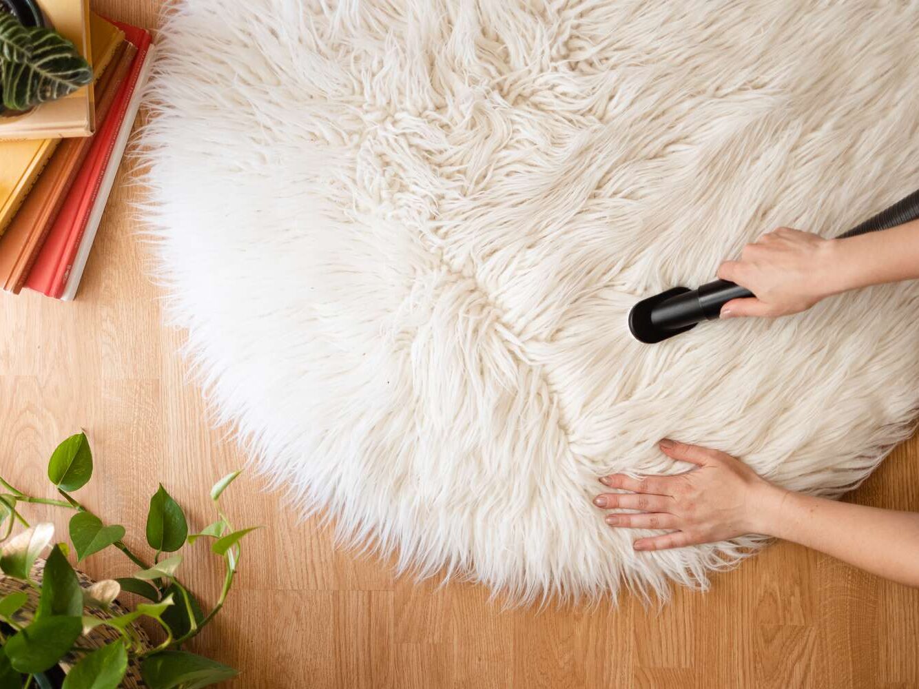 Person vacuuming a fluffy white round rug on a wooden floor.